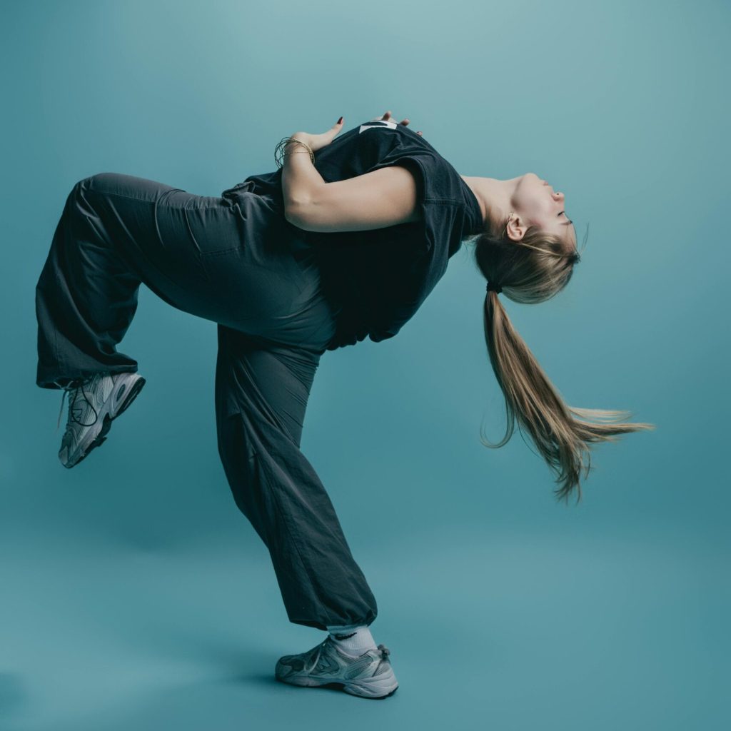 Young dancer captures motion in a dynamic pose with motion against a monochrome blue background.